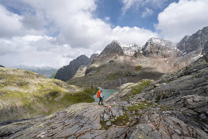 Mountaineer on a rocky hiking trail, view of the turquoise-blue mountain lake Großer Gradensee, behind her the summit of the Petzeck, Hoher Perschitzkopf and Kruckelkopf, Schober Group, Hohe Tauern National Park, Carinthia, Austria