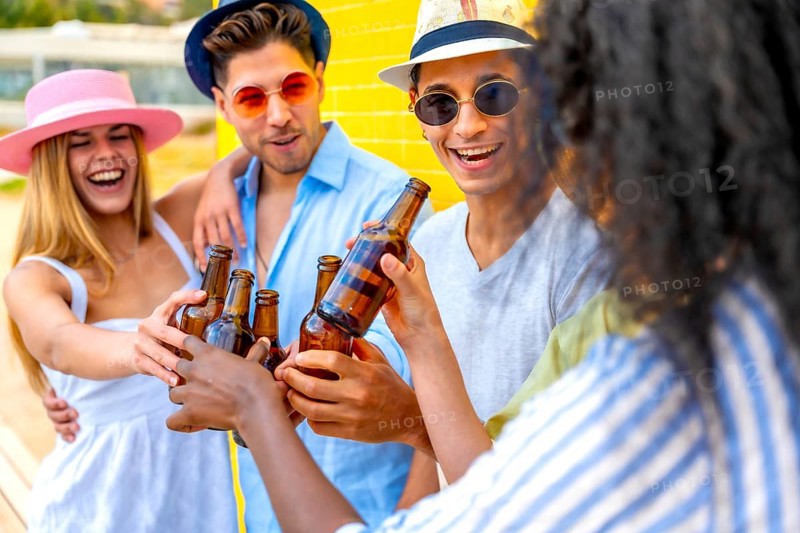Cheerful multi ethnic friends enjoying a summer party, toasting with beer bottles against a vibrant yellow wall