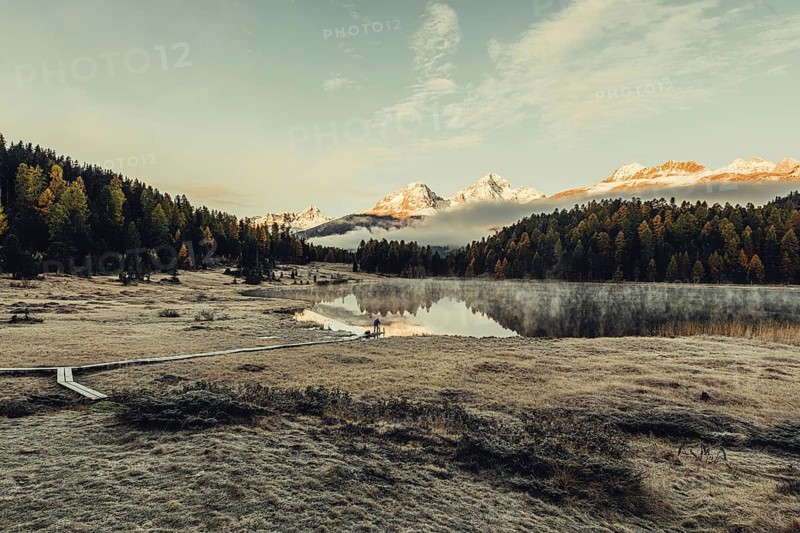 Lake Staz near Sankt Moritz in the Engadin in Switzerland. Morning atmosphere with fog in autumn. Water reflection and snow-covered mountains in the background