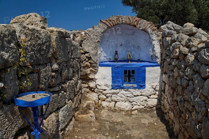 Stone chapel with blue window amidst ancient ruins, surrounded by natural walls and a deep blue sky, Artemis Temple, Artemis, Diana, goddess of the hunt, altar. Church, tower, near the airport in the north of the island, Leros, Dodecanese, Greek Islands, Greece
