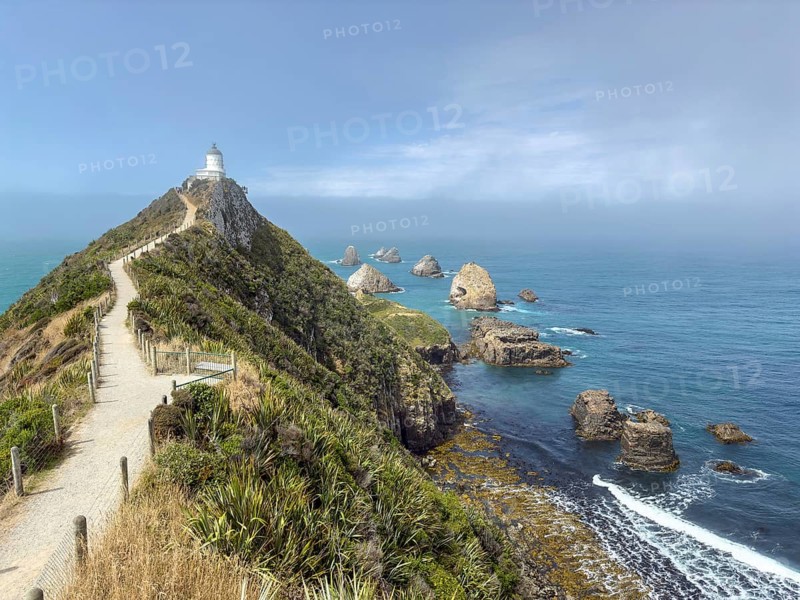 Nugget Point Lighthouse with Nugget Rocks in front of a blue sky, South Island, New Zealand, Oceania