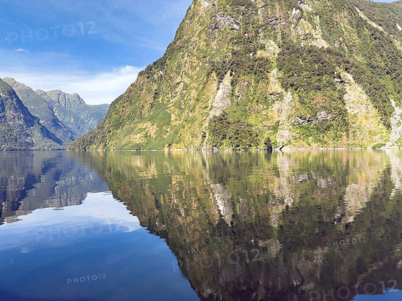 Mountains with reflections in the water against a blue sky in Doubtful Sound, South Island, New Zealand, Oceania