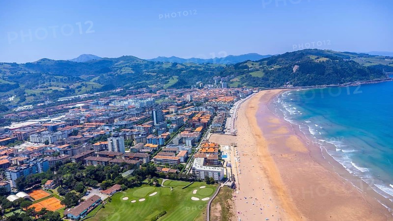 Aerial perspective of zarautz, gipuzkoa, showcasing the urban landscape meeting the sandy beach and blue ocean waves under a clear summer sky, Spain.
