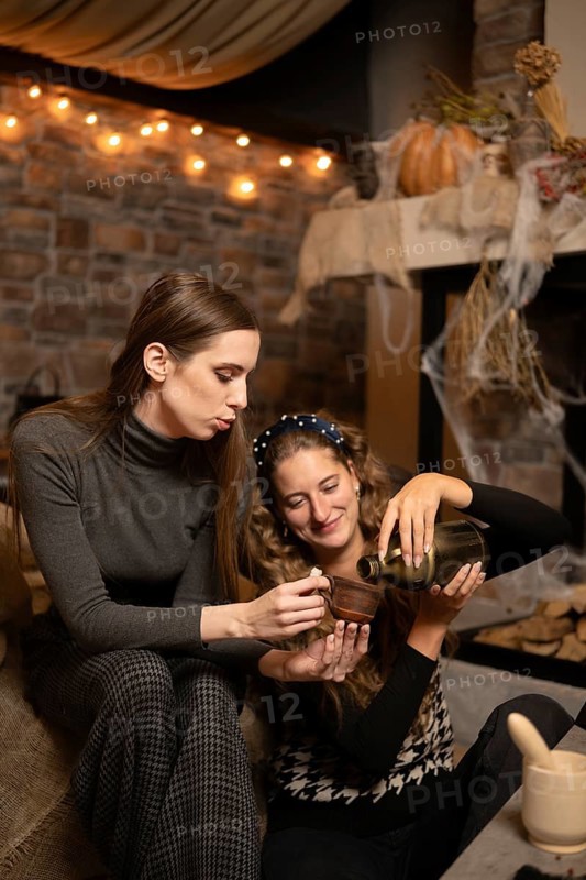 Two friends are seated together in a warm and inviting room, engaging in a joyful moment as one pours tea into a cup