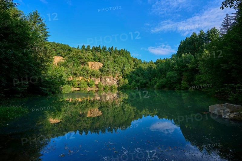 Tranquil lake in the middle of a forest with a clear water surface that reflects the sky, Katzenbuckelsee, Katzenbuckel, Waldbrunn, Neckar-Odenwald-Kreis, Odenwald, Baden-Württemberg, Germany