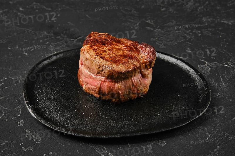 Perfectly seared filet mignon sits on a dark plate, highlighting its rich color and inviting look. The meat exhibits a mouthwatering crust, promising a tender and flavorful experience for diners
