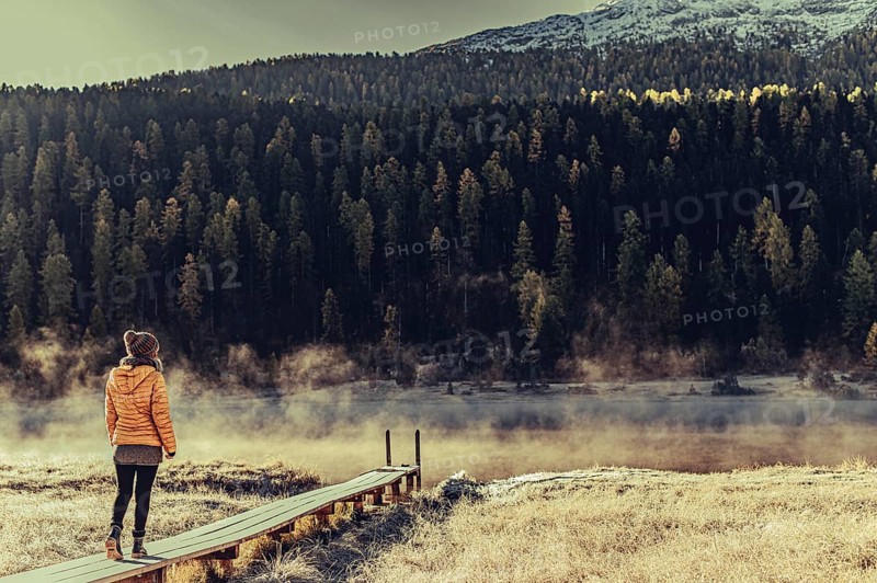 Young woman at Lake Staz near Sankt Moritz in the Engadine in Switzerland. Morning atmosphere with fog in autumn. Reflection of water