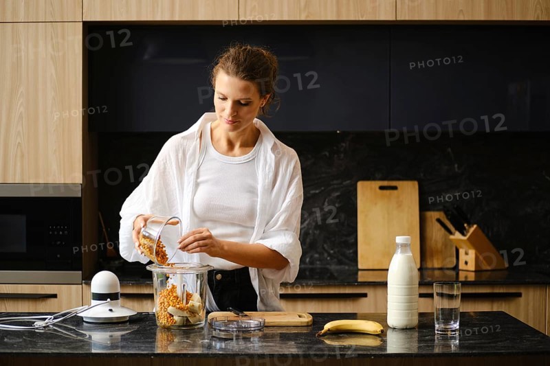 A woman is making healthy banana and sea buckthorn smoothies in a sleek kitchen