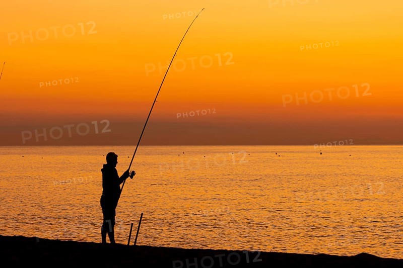 A man fishing just in front of sunrise on the Costa Rei, a coastline of the Italian island of Sardinia, in the Mediterranean Sea, Monte Nai, Costa Rei, Sardinia, Italy