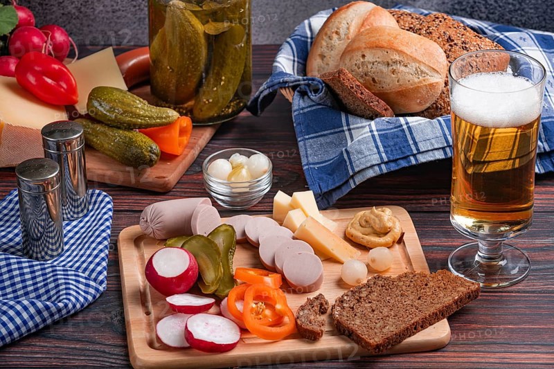 Rustic snack with sausage, cheese, beer, mustard, radishes and bread on a laid table