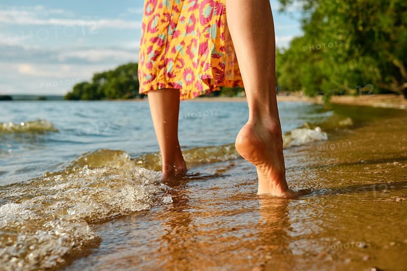 Low angle rear view of bare female feet on a calm beach. The gentle waves lap female feet