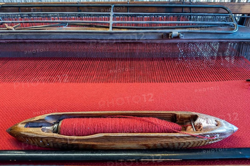 Old loom in the clothmaking museum in Bramsche, Lower Saxony, Germany, wooden shuttle on red fabric on a loom