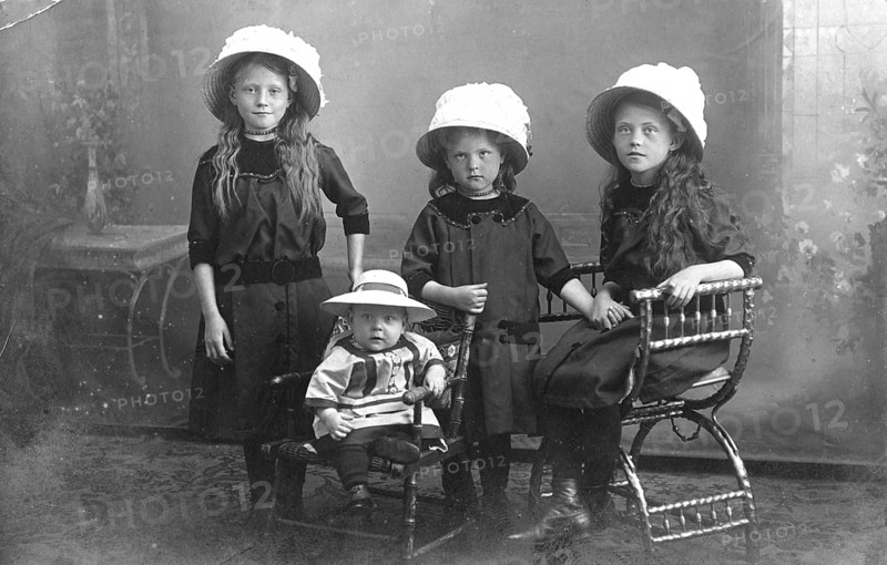 Three young girls with child, 1920s, Four girls wearing hats and dark clothes, standing and sitting in a nostalgic Victorian setting, Historical photo