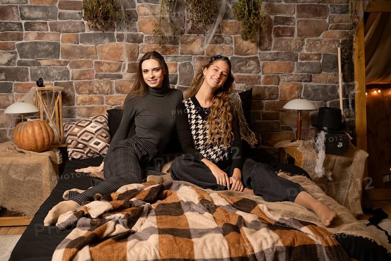 Two women enjoy a relaxed moment together on a warm blanket in a rustic bedroom filled with autumn decor