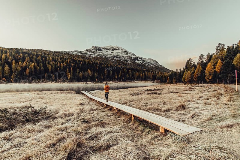 Young woman at Lake Staz near Sankt Moritz in the Engadine in Switzerland. Morning atmosphere with fog in autumn. Reflection of water
