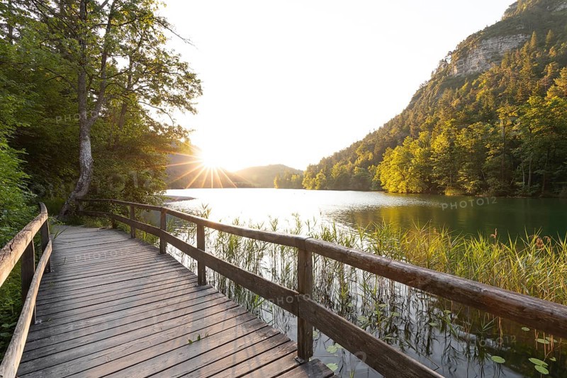Sunrise in summer at Lake Thumsee near Bad Reichenhall with a wooden footbridge and a sun star over the lake