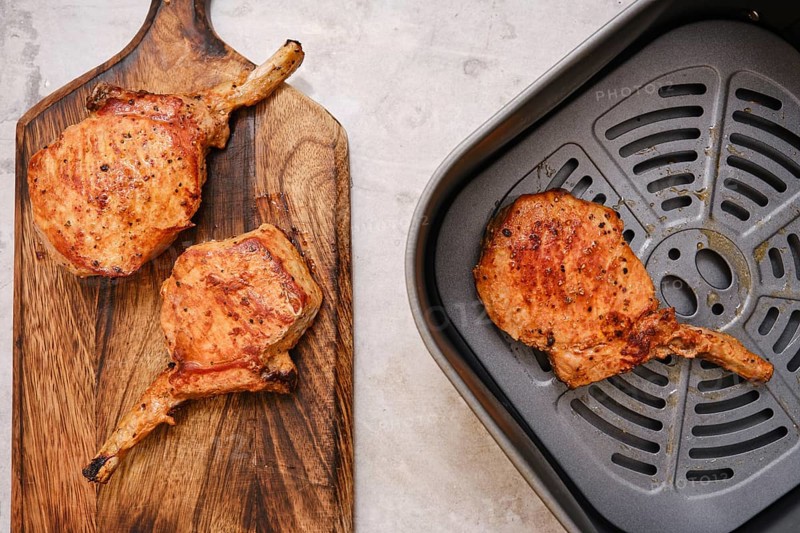 Juicy pork rib roasts are beautifully cooked to perfection, resting on a wooden cutting board. An air fryer sits nearby, ready for additional cooking or meal prep