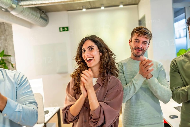 Group of smiling businesspeople applauding during a meeting in a modern office, celebrating success and teamwork