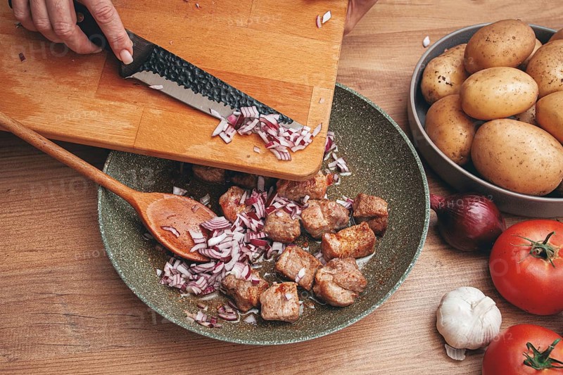 Adding chopped onion to the pan with meat, close-up