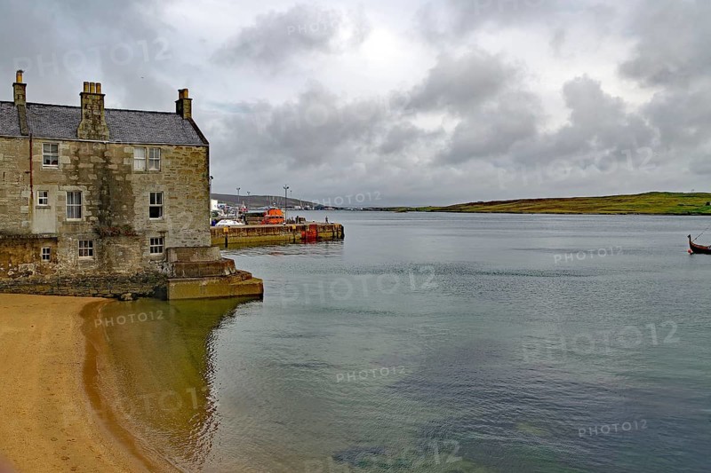 A stone cottage stands on the sandy shore of a calm loch under a cloudy sky, Lerwick, crime series, Shetland Islands, Scotland, United Kingdom