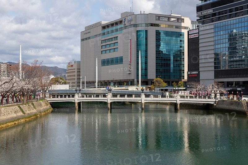 Tourist attraction, place of interest, riverside promenade with blossoming cherry trees, Sakura, modern architecture and historic Enkobashi stone bridge over the Enko River, Enko-bashi Bridge, built in 1926, restored in 2016 for the 70th anniversary of the atomic bombing, Enkobashicho, Minami Ward, Hiroshima, Japan