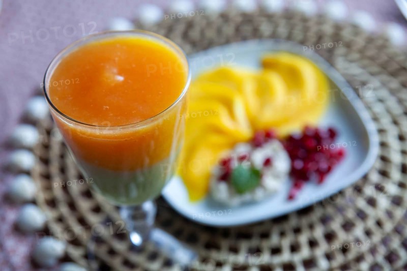 A glass with multi-coloured juice and a plate with mango slices and pomegranate seeds, Lower Austria Austria