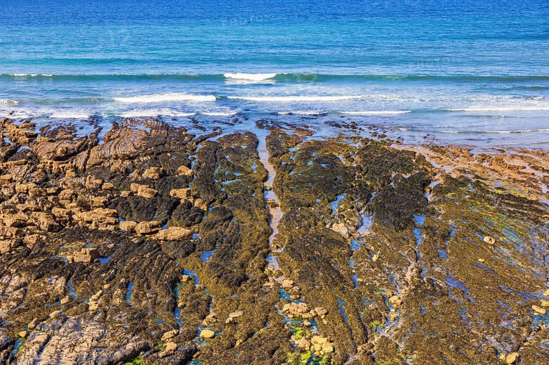Beach by the sea at low tide with water pools and waves crashing on the shoreline a sunny summer day, Crozon peninsula, Bretagne, France