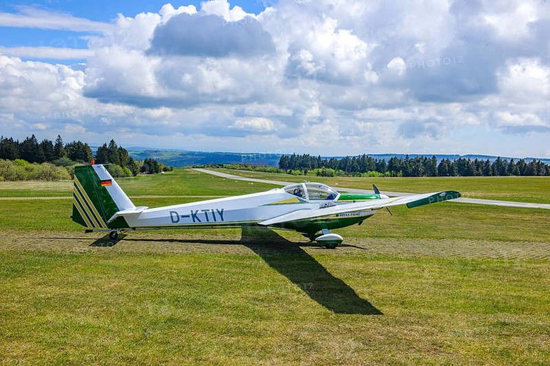Motor glider of the type Scheibe SF.25C Falke standing on Wasserkuppe airfield, in the background runway landing strip, Wasserkuppe airfield, Rhön, Gersfeld, district of Fulda, Hesse, Germany