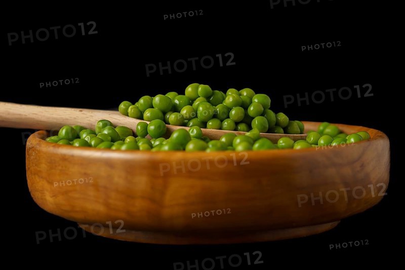 Wooden bowl with fresh peas and wooden spoon isolated on black background