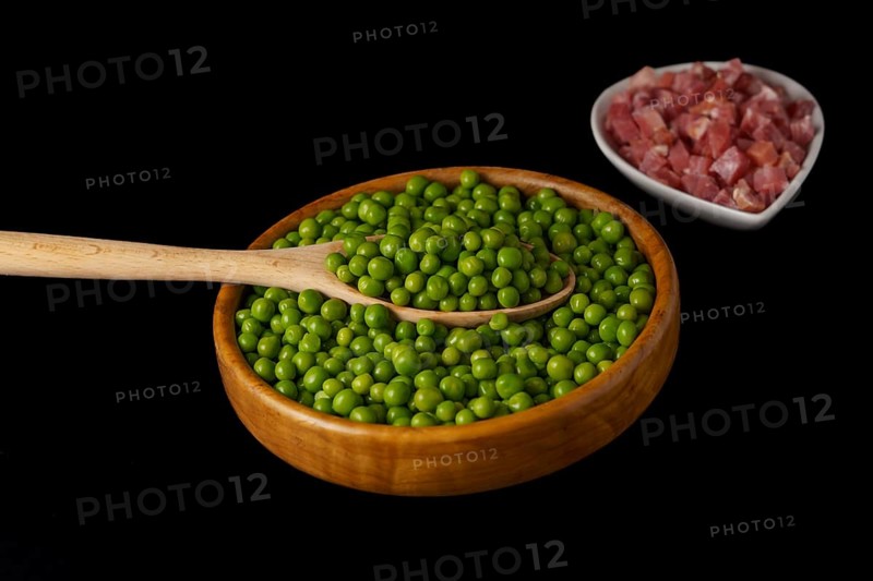 Wooden bowl with peas and white bowl with iberian ham isolated on black background