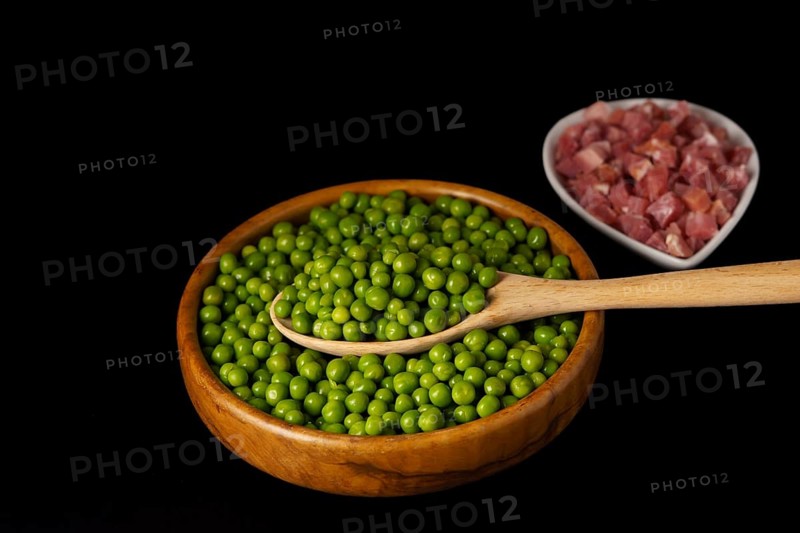 Wooden bowl with peas and white bowl with iberian ham isolated on black background