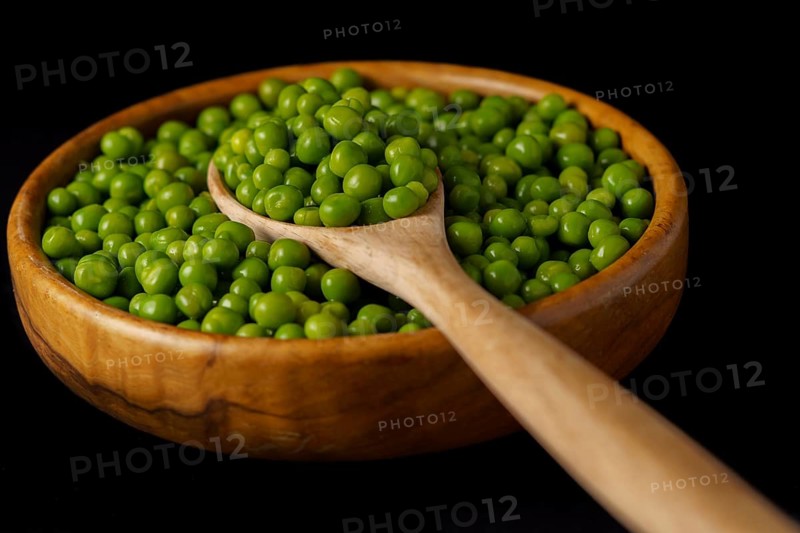 Wooden bowl with fresh peas and wooden spoon isolated on black background