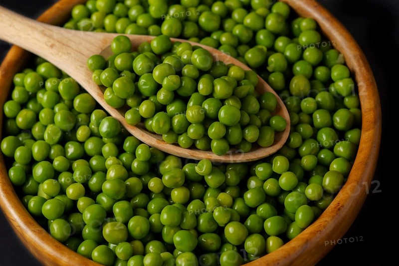 Wooden bowl with fresh peas and wooden spoon isolated on black background