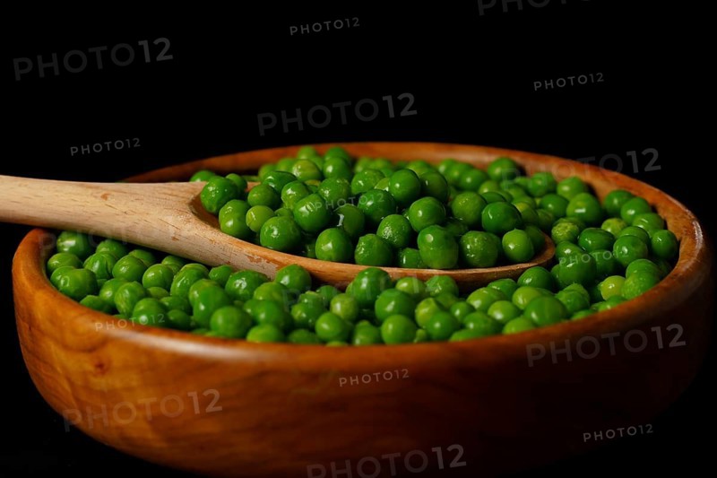 Wooden bowl with fresh peas and wooden spoon isolated on black background
