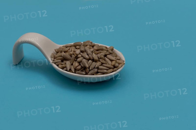 White ceramic spoon with peeled sunflower seeds and blue background