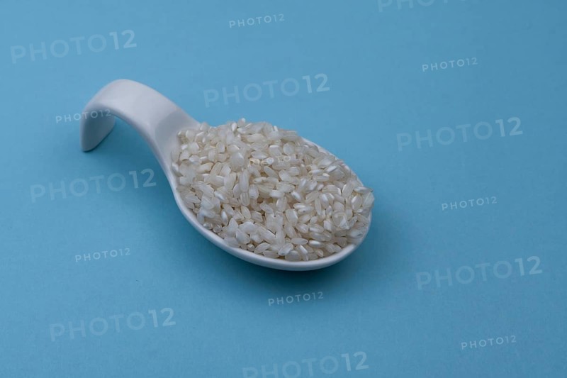White ceramic spoon with white uncooked rice and blue background