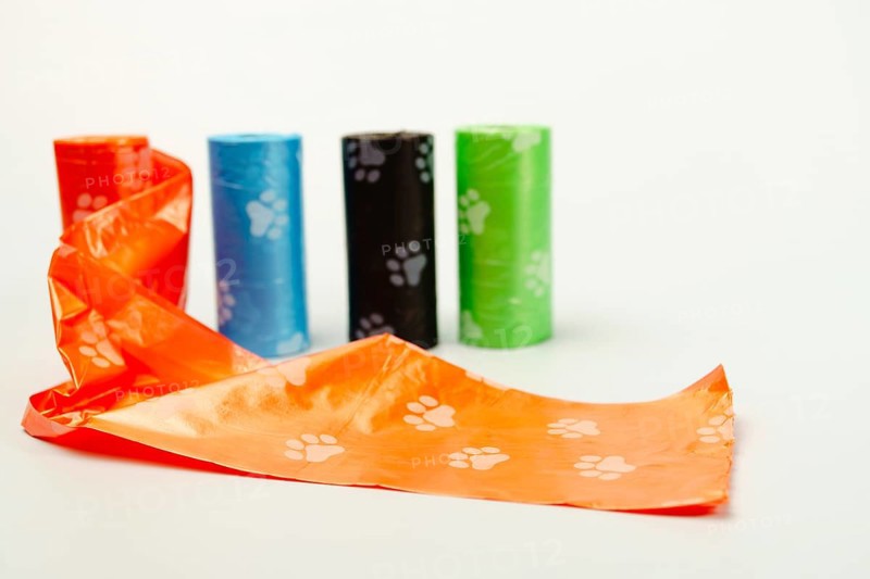 Orange dog poop bag unrolling with other colorful poop bags on a white background