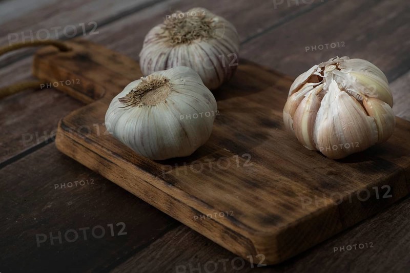 Whole and peeled garlic on wooden board and white background