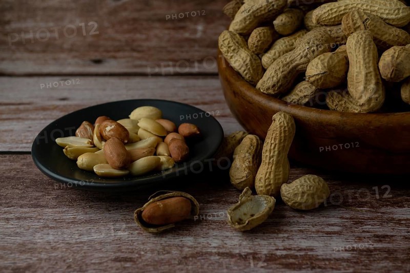 Peanuts in a wooden bowl and peeled peanuts on a plate with a spoonful of peanut butter