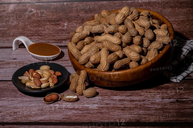 Peanuts in a wooden bowl and peeled peanuts on a plate with a spoonful of peanut butter