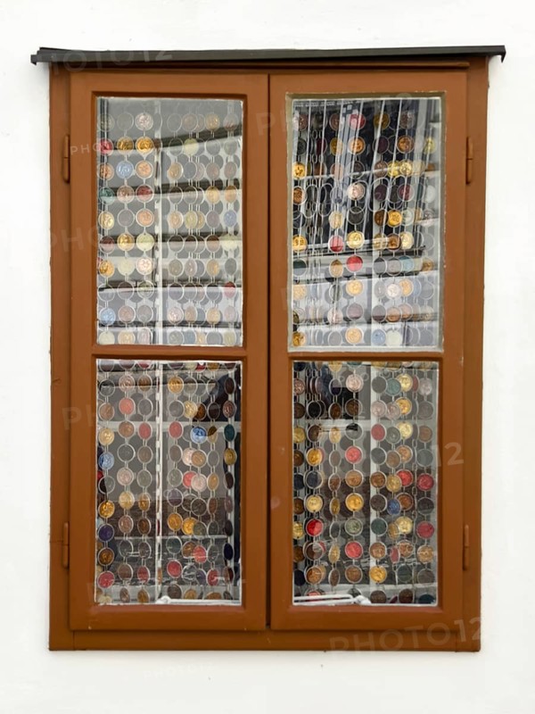 Window with decorative coin collection behind glass, framed by a simple wooden structure Mödling Lower Austria Austria