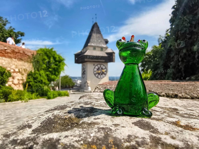 Green glass figure of a frog in front of historic clock tower
