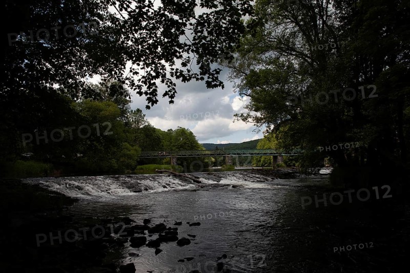 A dark river with a waterfall and bridge, surrounded by forests and cloudy skies Hardegg Weinviertel Lower Austria