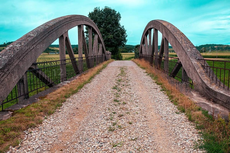 An old bridge with a gravel path leads through a rural area, surrounded by fields and a clear sky Perschling flood channel bridge Lower Austria Austria