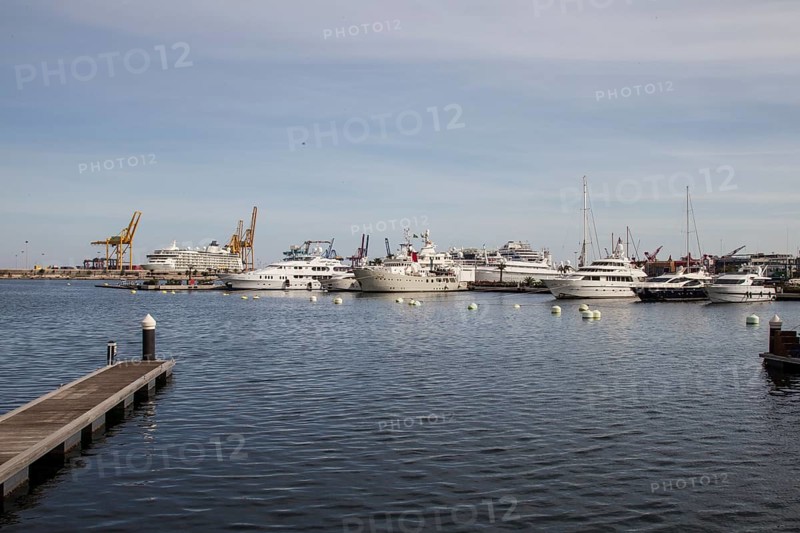 View of a busy harbour with yachts and industrial cranes in the background