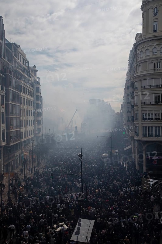 A large crowd gathers in a smoky city street MascletÃ¡ de Fallas