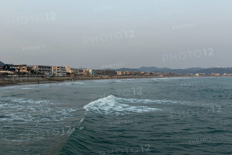 Houses on the seafront and surfers in the surf at dusk on the beach in Kamakura, Kanagawa Prefecture, Japan
