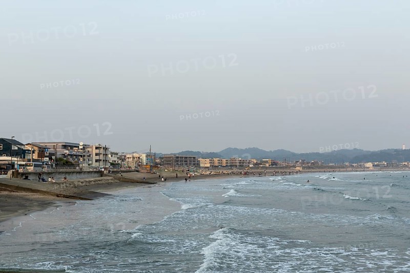 Houses on the seafront and surfers in the surf at dusk on the beach in Kamakura, Kanagawa Prefecture, Japan