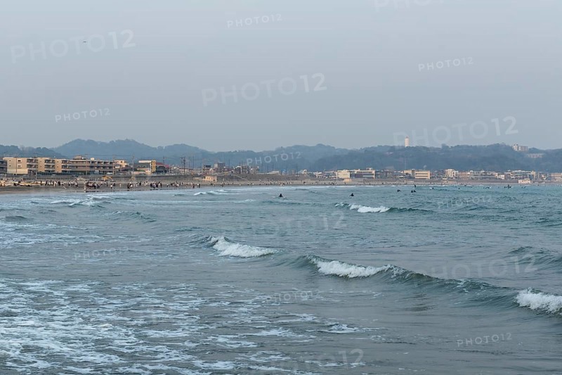 Houses on the seafront and surfers in the surf at dusk on the beach in Kamakura, Kanagawa Prefecture, Japan