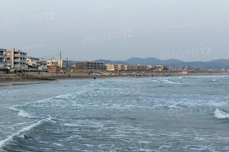 Houses on the seafront and surfers in the surf at dusk on the beach in Kamakura, Kanagawa Prefecture, Japan